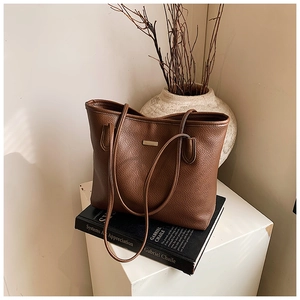 Detail of deep brown tote bag featuring pebble grain leather and metal nameplate on books