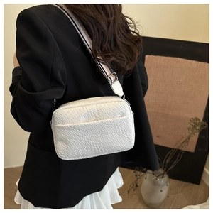 Detail view of white square crossbody bag with textured weaving and striped wide strap