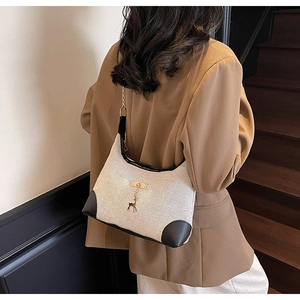 Detail of cream woven shoulder bag with black leather trim and gold deer pendant charm