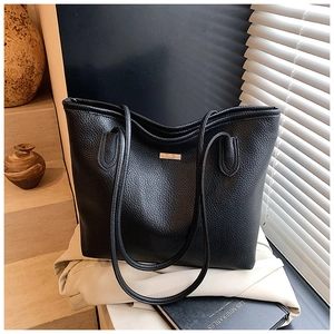 Detailed side view of black lychee grain leather tote bag with elegant metal plate accent