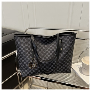 Detail of the large tote bag featuring M-letter monogram pattern and gold metal pendant