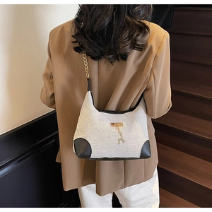 Detail of beige tweed tote bag with black leather trim and golden deer pendant on model