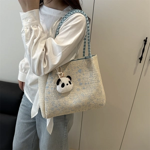 Blaue und beige gewebte Tragetasche mit Panda-Anhänger an der Schulter eines Models