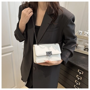 Detailed shot of white patent leather crossbody bag with a metal triangle buckle and chain