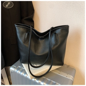 Close-up of black pebble leather tote bag with metal nameplate on silver suitcase