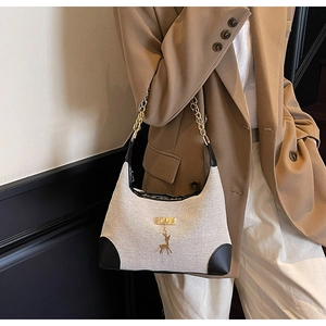 Detail of canvas tote bag with black leather trim, chain strap and gold deer pendant