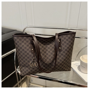 Macro shot of brown tote bag with M monogram pattern and metallic brand charm detail