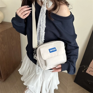 Chic off-white square crossbody bag with a blue brand label and wide fabric strap