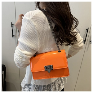 Détail d'un sac bandoulière orange vif en cuir verni avec fermoir en métal noir et chaîne