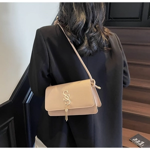 Detail of beige square crossbody bag with gold S-logo tassel and knotted strap