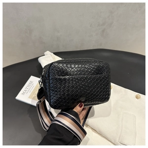 Detail of black woven camera bag featuring a wide striped canvas shoulder strap