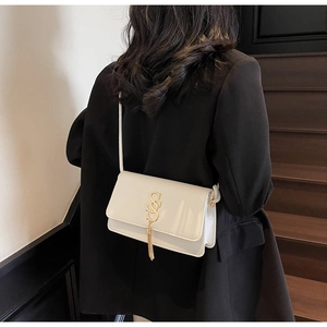 Close-up of a white square shoulder bag featuring a gold tassel and metal letter buckle
