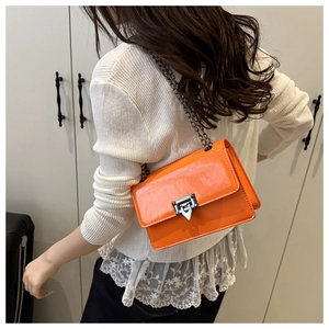 Detail of glossy orange patent leather shoulder bag with dark metal chain and lock