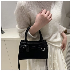 Détail du sac bandoulière noir avec boucle argentée porté avec une robe en tricot blanc