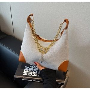 Detail of tote bag featuring beige weave texture, brown leather trim and golden deer charm