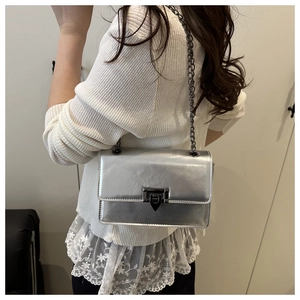 Détail du sac bandoulière argenté brillant avec chaîne sombre et fermoir géométrique