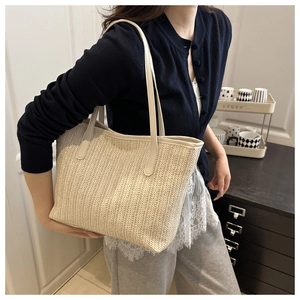 Straw tote bag with herringbone weave and leather handles shown on a shoulder