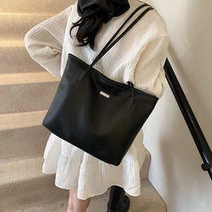 Minimalist black pebbled leather tote bag with slim shoulder straps shown on a model