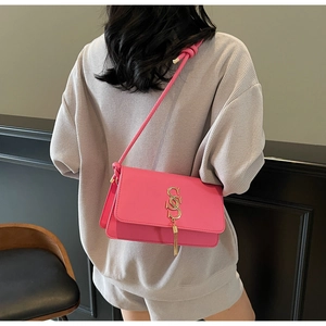 Detail of pink crossbody bag with golden tassel charm and metal letter on square flap