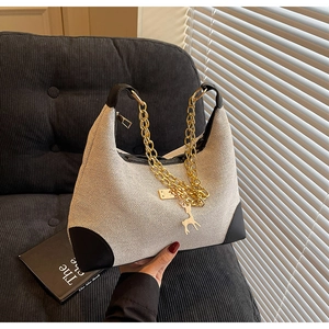 Detail of cream canvas hobo bag with black leather trim and gold chain on corduroy