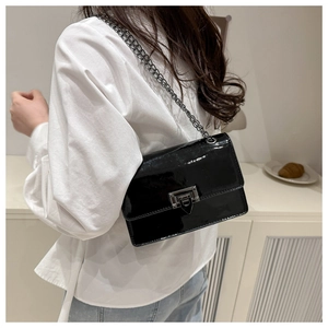 Détail de la surface en cuir verni noir brillant avec chaîne en métal et fermoir rotatif