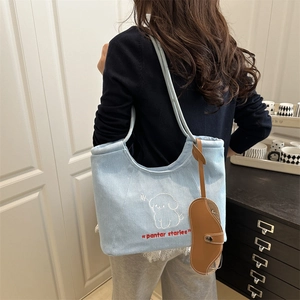 Blue denim tote bag with cute puppy embroidery and long shoulder straps worn by a model