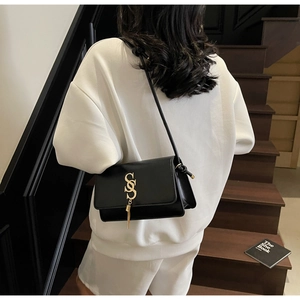 Close-up of minimalist black leather crossbody bag with gold SS lock and tassel detail