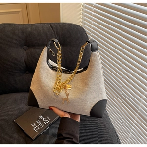 Detailed shot of beige woven hobo bag featuring black leather trim and gold deer charm