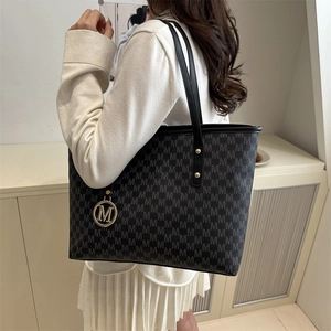 Large grey tote bag with M-letter pattern and gold charm shown on model in modern setting