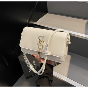 Detail of white square bag with golden S-logo, metallic tassels and knotted strap