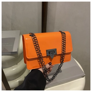 Détail d'un sac carré en cuir verni orange vif avec chaîne métallique et fermoir design
