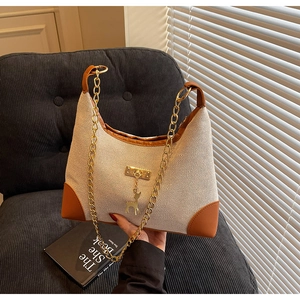 Detail of woven tote bag featuring brown leather trim and a golden deer charm