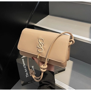Detail of beige square crossbody bag with gold S-buckle, fringe, and knotted rope strap
