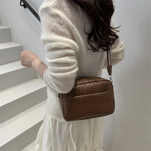 Brown woven texture crossbody camera bag with striped fabric strap on white stairs