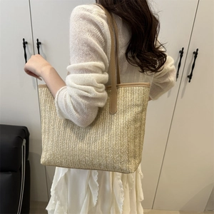 Minimalist straw woven tote bag with khaki leather trim worn by model in a warm room