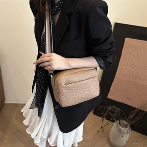 Khaki woven texture crossbody bag with stylish wide strap worn by a woman in a black blazer
