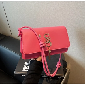 Detail of hot pink crossbody bag with golden S-shaped logo and elegant chain tassel
