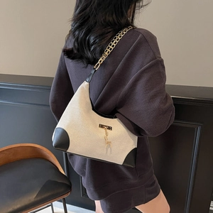 Chic beige canvas shoulder bag with black leather corners and gold chain strap shown on model