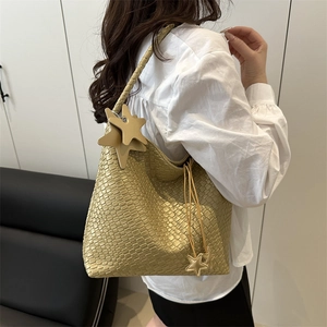 Champagne gold woven tote bag with star charms shown on shoulder in a modern setting