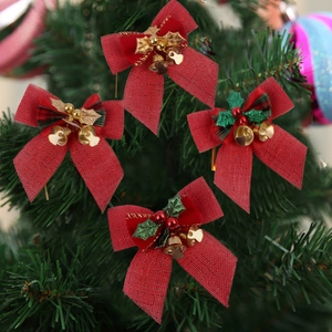 Close-up of four red burlap Christmas bows with gold bells and holly berries on a tree