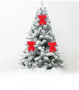 Close-up of three red satin Christmas bows with gold trim hanging on a snowy tree