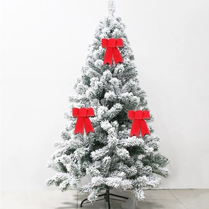 Three red velvet Christmas bows with gold trim hanging on a white frosted pine tree branch
