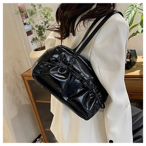 Dettaglio borsa a spalla in pelle verniciata nera con fiocco arricciato su blazer bianco
