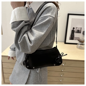 Detail of a black leather underarm bag with ribbon bows and silver metal studs
