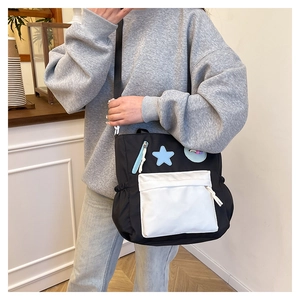 Detail of star-shaped patches and contrast front pocket on black canvas shoulder bag