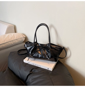 Detailed view of black dumpling bag with bow decoration and pleated texture on books