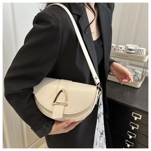 Detail of cream white leather saddle bag featuring a gold triangle clasp on a model