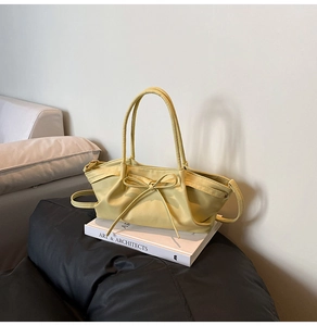 Detail of a lemon yellow croissant bag with a decorative bow on minimalist background