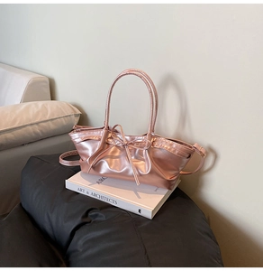 Detail of rose gold metallic dumpling bag featuring pleated texture and bow decoration