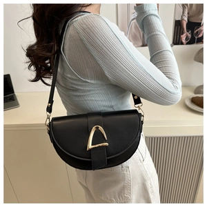 Detail view of a black saddle bag with a gold D-buckle worn as a crossbody shoulder bag